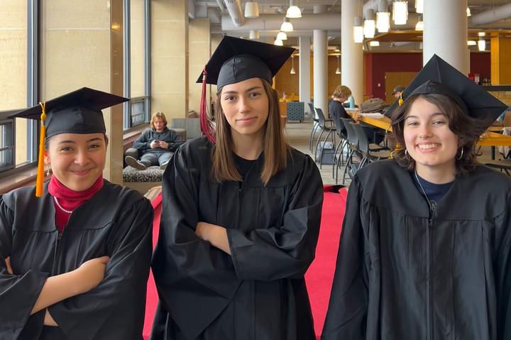 3 female college students standing next to each other in relaxed poses wearing black graduation caps and gowns